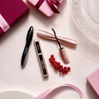 Подредба отгоре на грим продукти Lancome, включваща спирала и гланц за устни, заедно с розови подаръчни кутии, сатенени панделки и стръкче френско грозде.