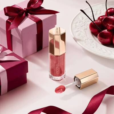 Гланц за устни Lancome в нюанс горски плодове в луксозен шестоъгълен флакон, аранжиран с подаръчни кутии и череши.