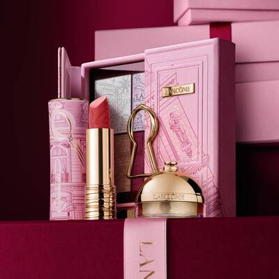 Изискан празничен подаръчен комплект Lancome, съдържащ червило, палитра сенки за очи и златни бюти продукти, аранжирани до декоративна розова кутия.