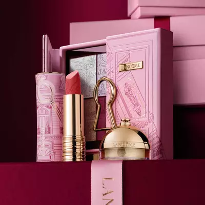 Изискан празничен подаръчен комплект Lancome, съдържащ червило, палитра сенки за очи и златни бюти продукти, аранжирани до декоративна розова кутия.