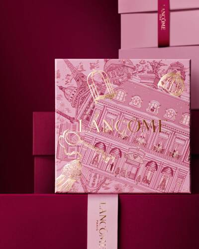 Снимка на розова празнична подаръчна кутия Lancome на фона на поредица от розови и тъмночервени кутии върху тъмночервен фон.