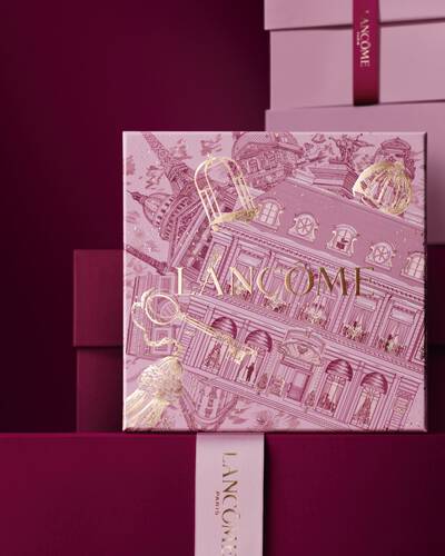 Изображение на розова празнична подаръчна кутия Lancome пред купчина розови и тъмночервени подаръчни кутии на тъмночервен фон.