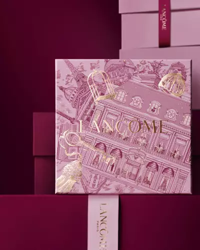 Изображение на розова празнична подаръчна кутия Lancome пред купчина розови и тъмночервени подаръчни кутии на тъмночервен фон.