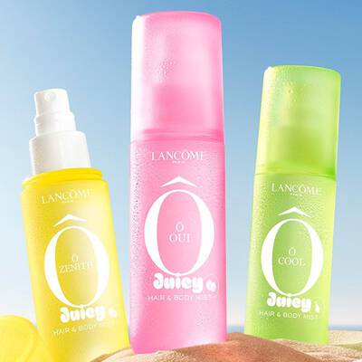 Три Lancome Juicy Hair & Body Mists в ярко жълто (O Zenith), розово (O Oui) и зелено (O Cool) стоят на пясъчен плаж.