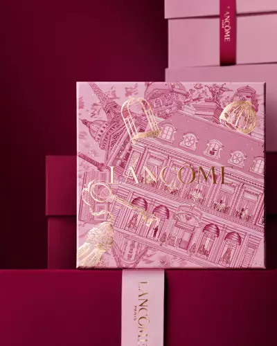 Изображение на розова празнична подаръчна кутия Lancome пред купчина розови и тъмночервени подаръчни кутии на тъмночервен фон.
