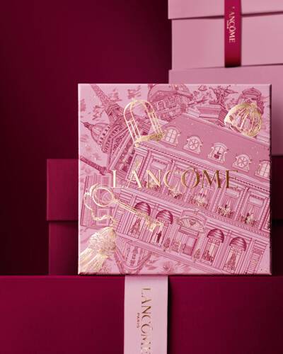 Изображение на розова празнична подаръчна кутия Lancome пред купчина розови и тъмночервени подаръчни кутии на тъмночервен фон.
