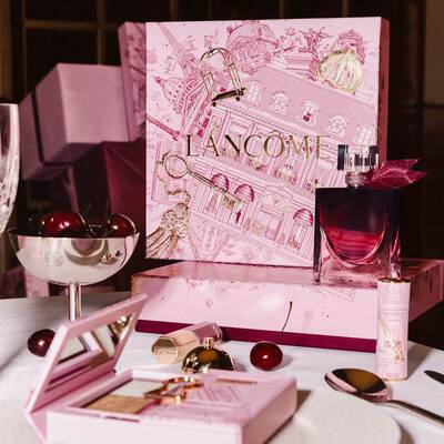 Тържествено представяне на празничната колекция на Lancome върху маса с голяма розова кутия с авторски илюстрации, парфюм, грим продукти и свежи череши.
