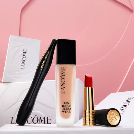 Ръка държи козметични продукти на Lancome, разположени на бели кутии с розов фон.