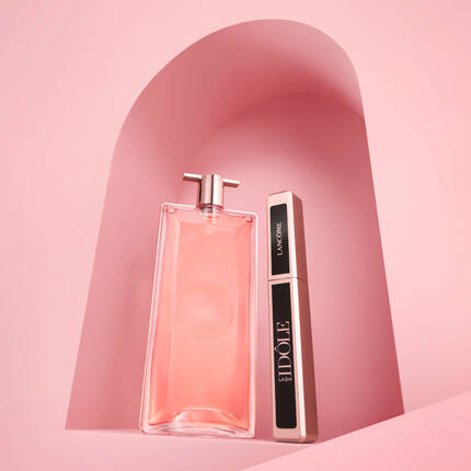 Два козметични продукта, флакон с розов аромат и спирала, подредени на розов фон с абстрактна форма.