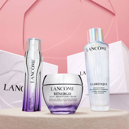 Три продукта за грижа за кожата на Lancome, включително крем и серум, подредени на розов фон с опаковки.