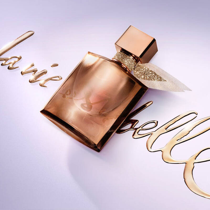 Флакон за парфюм в златисто с надпис "La Vie Est Belle" на светъл фон.