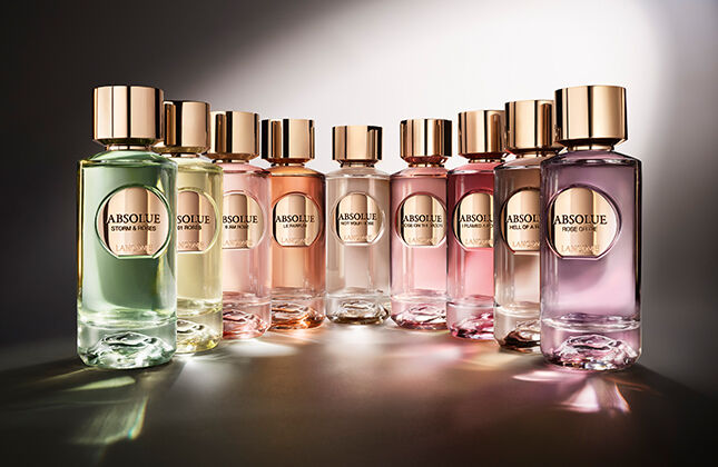 A collection of elegantly designed perfume bottles arranged in a row, featuring various colors and a soft, illuminated background that enhances their sleek appearance.