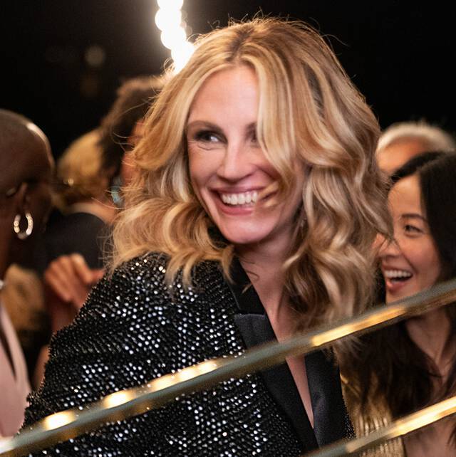 A group of people smiling and enjoying themselves at an event, with one person in the foreground wearing a sparkling black jacket.