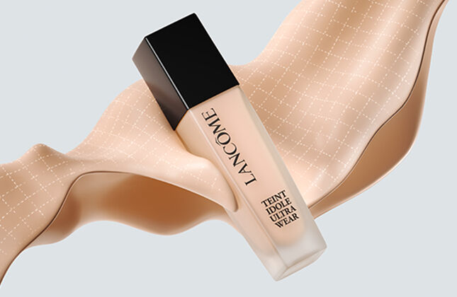 A bottle of foundation positioned on a flowing ribbon-like fabric in a soft beige tone, set against a light background.