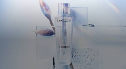 Алт текст: Стилен флакон с лосион Lancome Clarifique, разположен на светъл фон с графични елементи и близък план на пъпки и капчици вода.