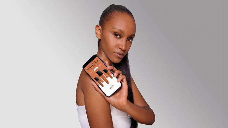 Млада жена с дълга коса държи смартфон, който показва цветове на козметични продукти.