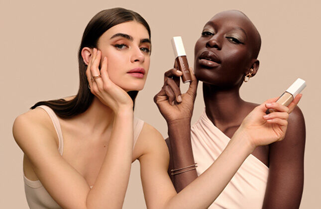 A stylish arrangement of Lancome cosmetics, including a liquid eyeliner, a foundation bottle, and a bold red lipstick, set against a warm gradient background.