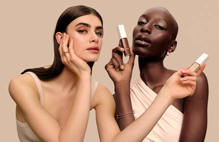 A stylish arrangement of Lancome cosmetics, including a liquid eyeliner, a foundation bottle, and a bold red lipstick, set against a warm gradient background.
