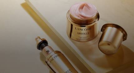 Крем и серум от Lancome в златиста опаковка, разположени на блестяща повърхност.