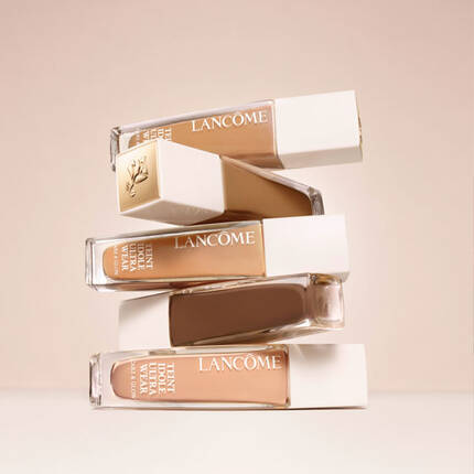 Четири флакона фон дьо тен на Lancome, подредени един върху друг на светъл фон.