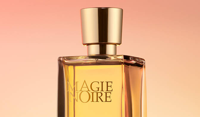 A glass perfume bottle with a gold cap, displaying the label "MAGIE NOIRE," against a soft gradient background in warm shades.