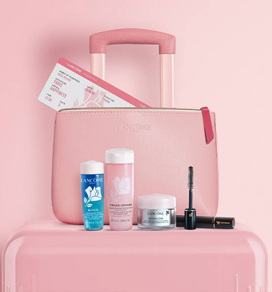 A pink Lancome travel bag with a suitcase handle, featuring a set of beauty products: a blue cleansing gel, a pink toner, a cream, and a mascara, along with two beauty event tickets. The background is a soft pink.