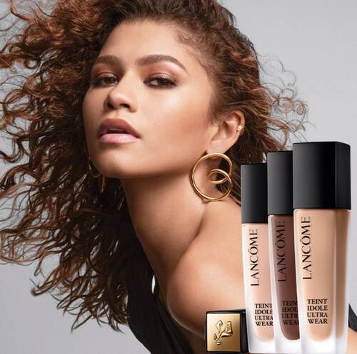 Млада жена с къдрави коси позира заедно с фон дьо тен на Lancome.