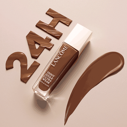 A tube of foundation resting on a smooth surface, accompanied by a swatch of the same shade and stylized text spelling "Makeup". The background is a soft, neutral color.