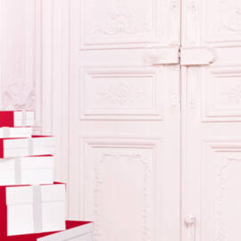 Stacks of red and white gift boxes are placed in a softly lit, elegant room with light-colored walls and ornate details.