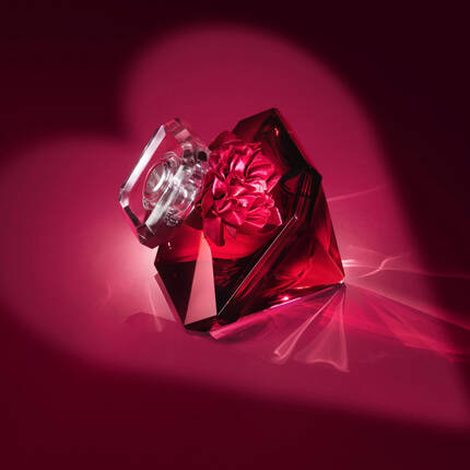 A decorative perfume bottle with a crystal lid and a flower design on a deep red background, creating a romantic and luxurious atmosphere.