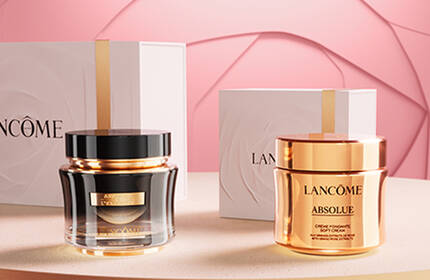 Elegant display of Lancome skincare products on a soft pink background, featuring a luxurious cream in a golden jar and a serum in a sleek bottle, both accompanied by stylish packaging.