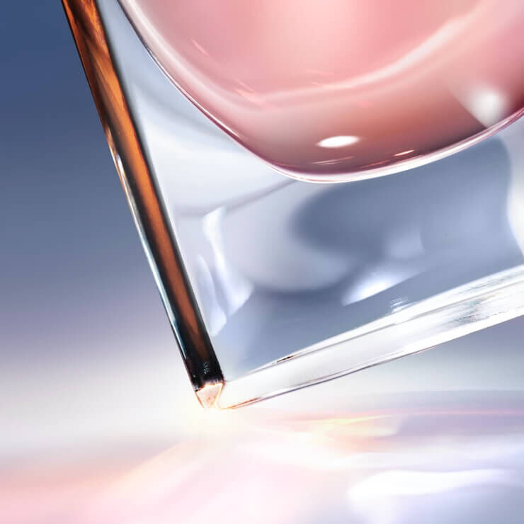 Изображение на стилна чаша с розов течност, която е наклонена и отразява светлина.